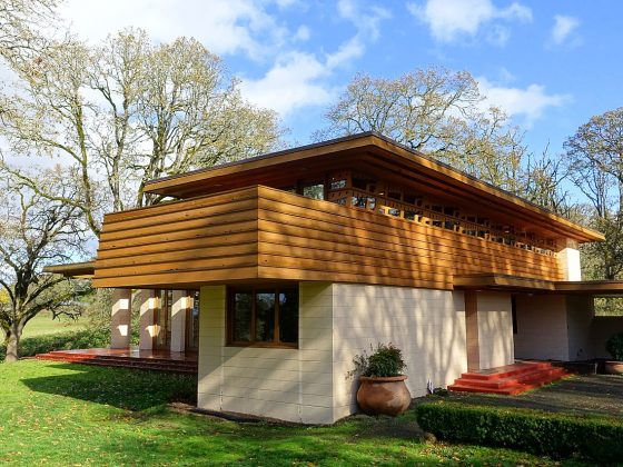 The exterior of a rectangular two-level house with half cement blocking and half wood paneling. Trees behind the house.