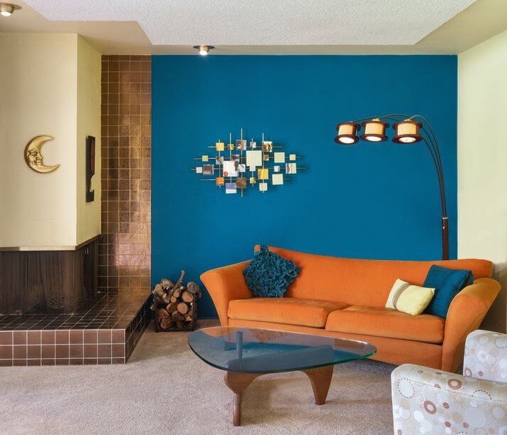 The living room of the "Garden Penthouse," complete with an orange sofa, three-bulbed lamp, and glass wall mosaic.