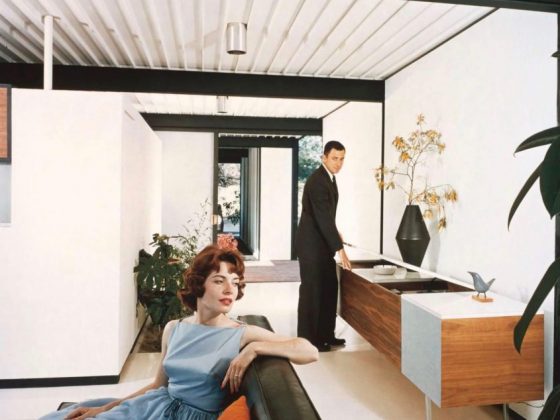 A woman reclining on a couch while a man stands at a table in the iconic Bailey House.