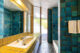 This bathroom features a blue tiled shower, yellow tiled countertops, and a hexagon tiled floor.